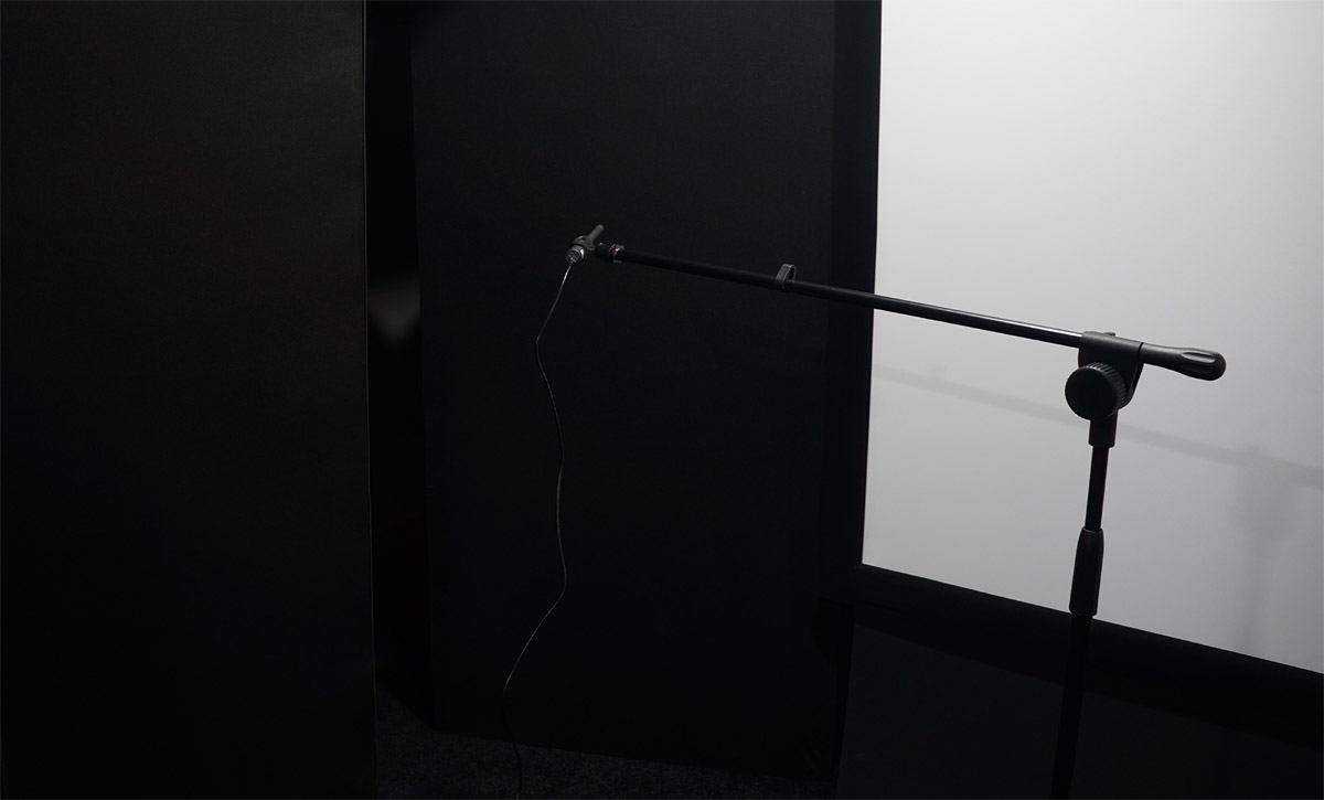 Le banc de mesure : microphone de mesure calibré sur pied télescopique, pointé vers un tissu sombre tendu sur cadre, à contre-jour
