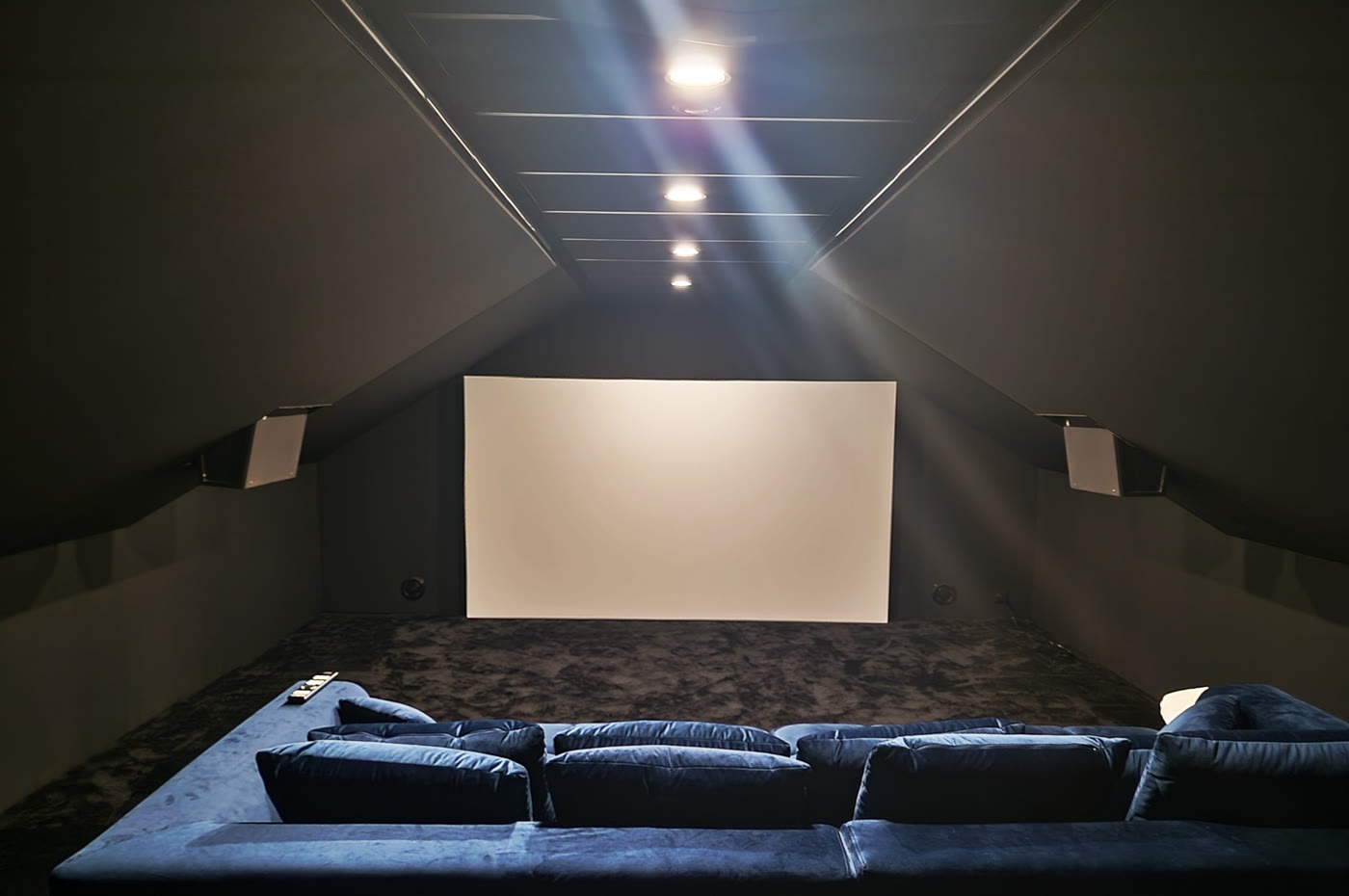 La salle de cinéma privée de Steven, sous les combles : écran, enceintes latérales en applique sur les rampants et gradins